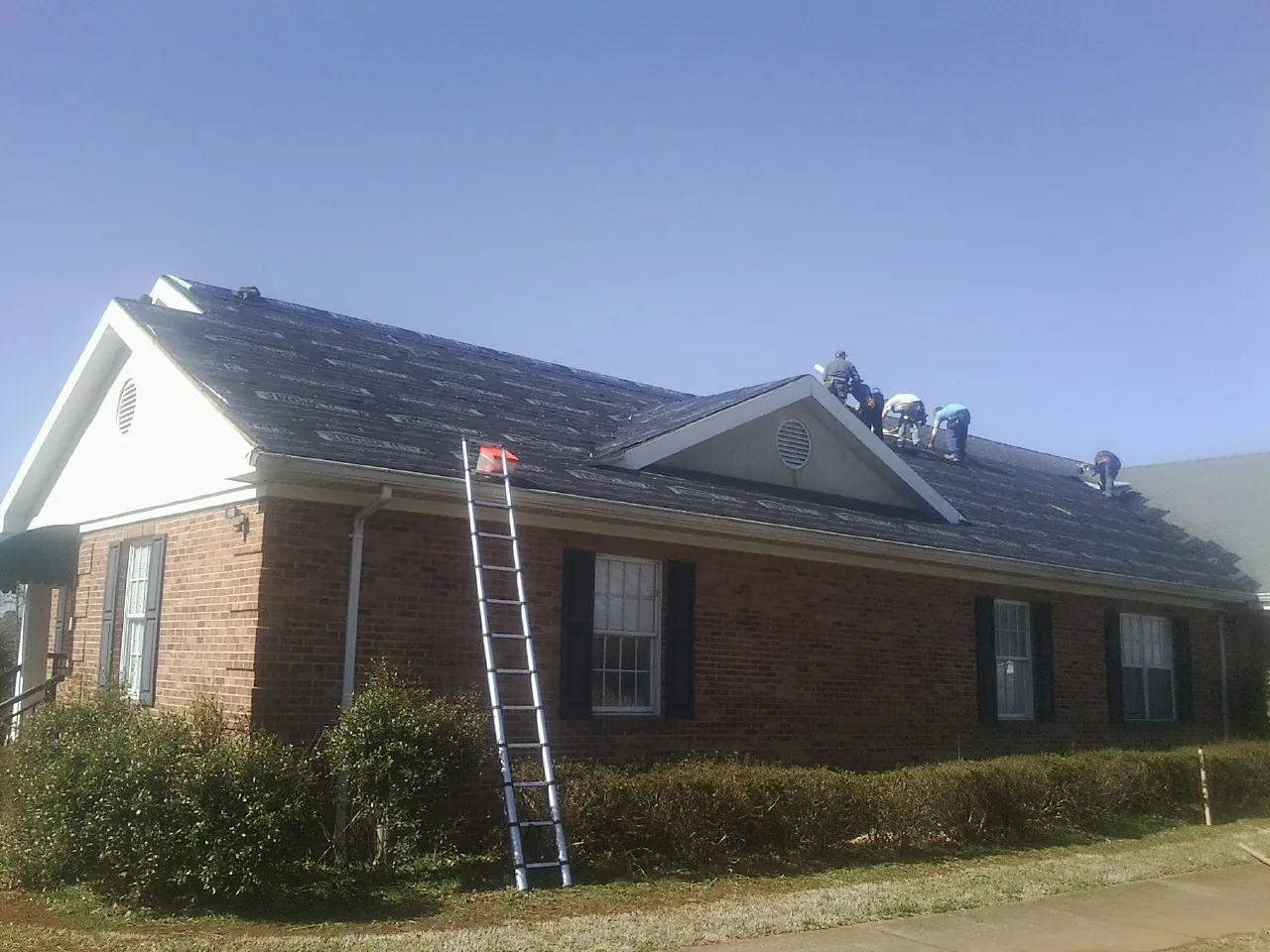 Crew tearing shingles off a brick ranch roof with a ladder set — Metal Roof Repair work by our crew in Oriskany Falls
