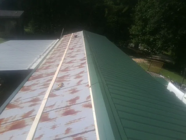 Old rusted panels beside newly installed green metal roofing — Wind Damage Roof Repair by Roofing Brothers in Oriskany Falls