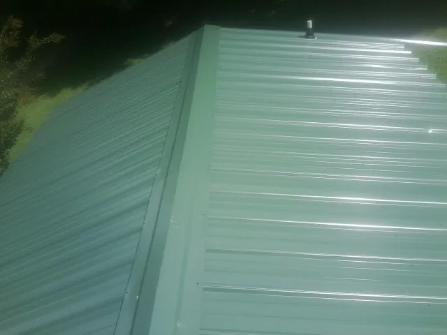 New green metal panels meeting at the ridge of a roof — Flat Roof Repair work by our crew in Oriskany Falls