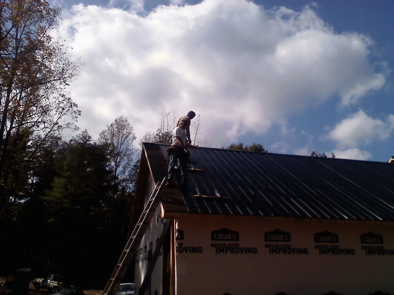 Roofer fastening dark metal panels high against a cloudy sky, from a Roof Inspection job in Oriskany Falls