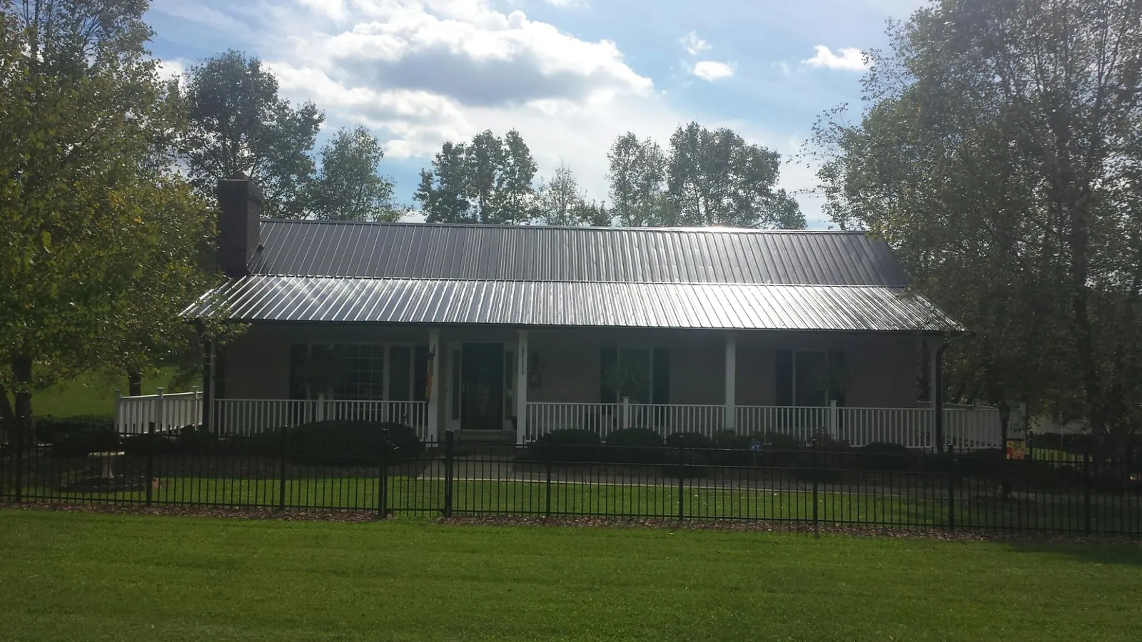 Gray metal roof on a brick ranch with a full width front porch — Gutter Guard Installation work by our crew in Oriskany Falls