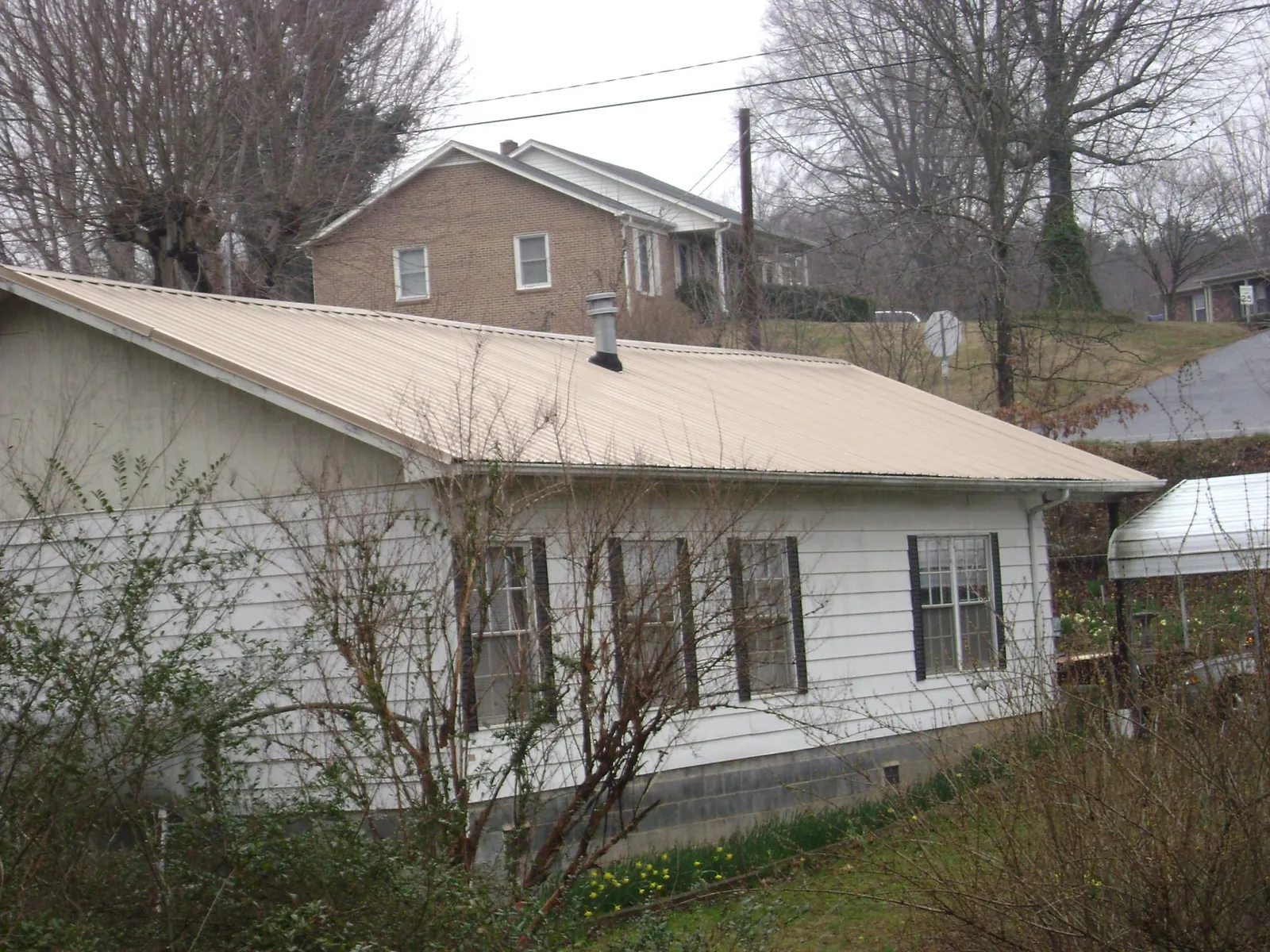 Tan metal roof on a white sided house set into a hillside — Commercial Roofing by Roofing Brothers in Oriskany Falls