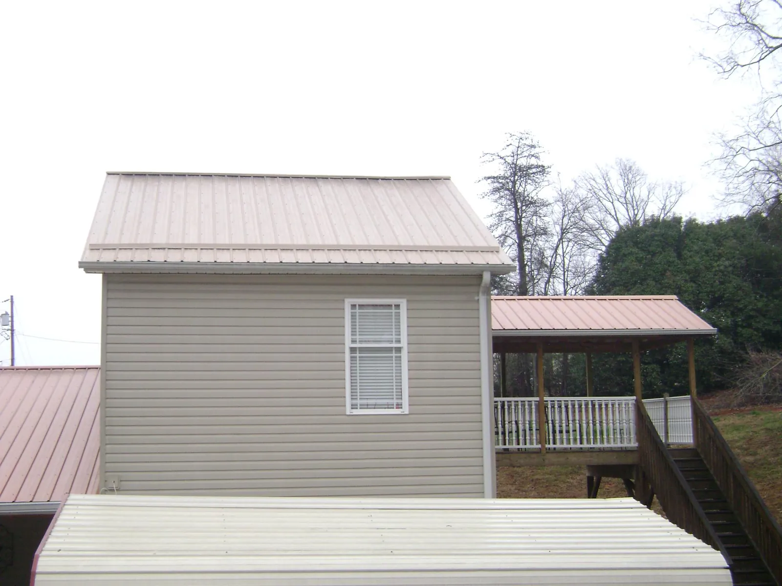 Tan metal roofs on a two story addition and attached porch, from a Roof Replacement job in Oriskany Falls